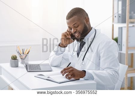 Young African Doctor Talking To Patient On Phone While Working In Modern Clinic, High Quality Servic