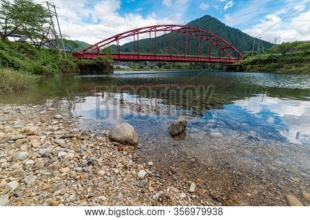 Red Bridge And River In The Mountain Valley. Japanese Countryside Landscape. Atera Valley In Kiso Va