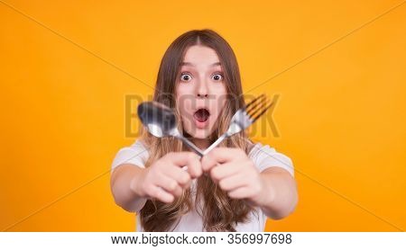 Frightened And Unhappy Young Caucasian Girl Crossed A Fork And A Spoon In Her Hands, Focus On The Fa