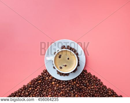 Flat Lay. White Ceramic Cup With Aromatic Coffee On A Hill Of Coffee Beans On A Pink Background. Cof