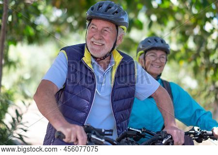 Beautiful Active Senior Couple With Electrobikes Standing Outdoors In The Park. Two Happy Elderly Pe