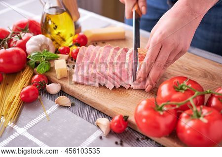 Womans Hands Slicing Pancetta Ham Bacon On Wooden Cutting Board At Domestic Kitchen