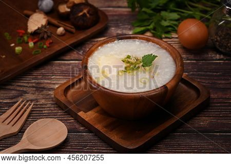 Rice Porridge Or Congee With Soft Boiled Egg, Slice Ginger And Slice Scallion Topping On Wooden Tabl