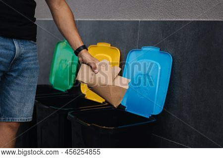 Close-up Of Man Throwing Peace Of Cardboard In Recycling Bins. Humen Hand Holding Paper Near The Pla