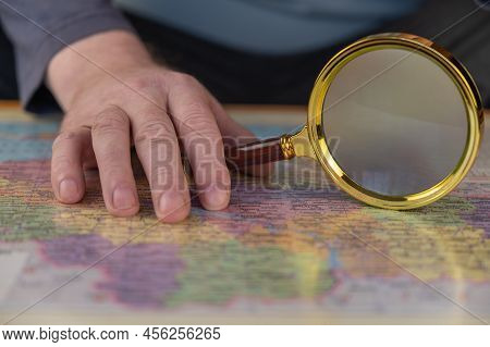 A Man Holds A Magnifying Glass In His Hand Over A Map. A Middle-aged Man With A Magnifying Glass In 