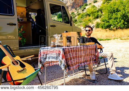 Man In Charming Trailer House Makes Coffee Outdoors In Mountains In Summer Sunny Day