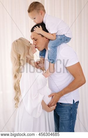 Dad Hold His Son On Neck And Hug His Pregnat Wife. Family Look Concept For Studio Photosession. Pere