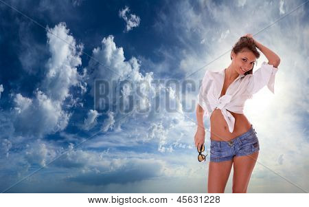 Ung kvinde i jeans shorts stående på blå skyet himmel backgroound