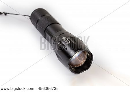 Modern Tactical Electric Led Flashlight In Black Housing With Zooming Of The Light Beam On A White B
