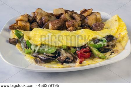 Omelet Filled With Onions Mushrooms And Peppers And Served With Homefries