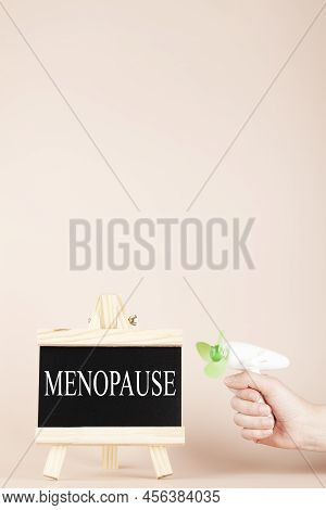 Menopause Word Written On Black Board And Hand Holding Fan On Beige Background. Women Health And Mid