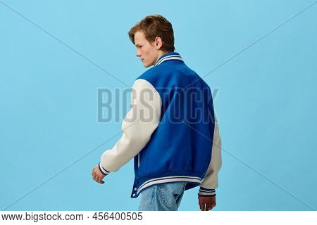 A Handsome, Young Man Student In A Trendy Blue Bomber Jacket Stands With His Back To The Camera On A