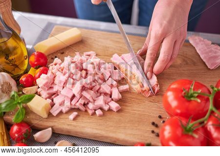 Womans Hands Slicing Pancetta Ham Bacon On Wooden Cutting Board At Domestic Kitchen