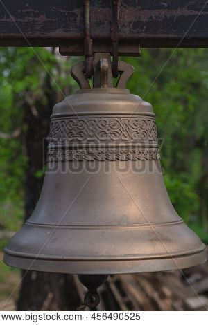 Side View Close-up Of Russian Church Bell Outdoors On Green Blurred Background, Summer Evening.