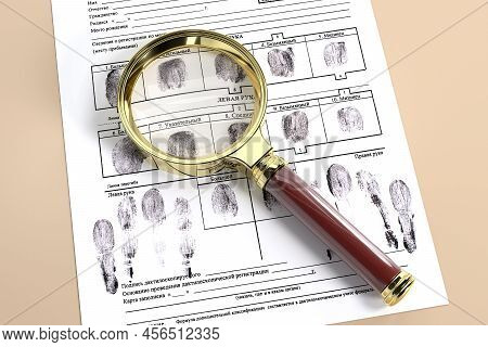 The Magnifying Glass Lies On A Fingerprint Card With Fake Fingerprints. On The Form, The Names Of Th