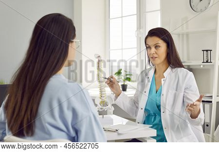 Female Doctor Talking To Patient Points To Vertebrae On Spine Model Telling Principle Of Treatment.