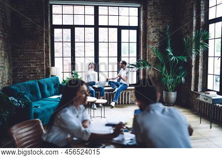 Young Asian Female Sitting On Windowsill And Laughing While Working Using Laptop During Work In Crea
