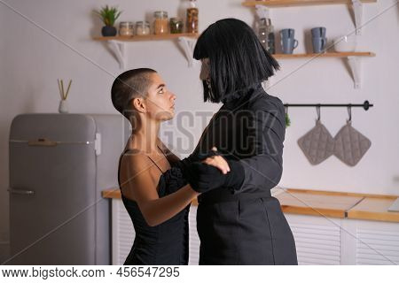 Young Woman Dances With Masked Man, Cosplay For Film Vendetta. Girl In Black Dress With Short Hair W
