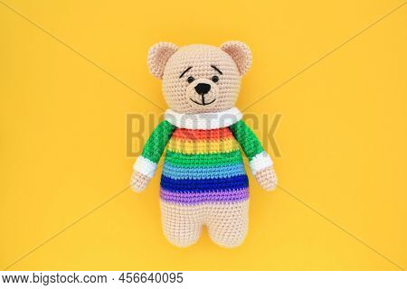 Crochet Amigurumi Handmade Stuffed Soft Teddy Bear Toy In Rainbow Sweater On Yellow Background. Hand