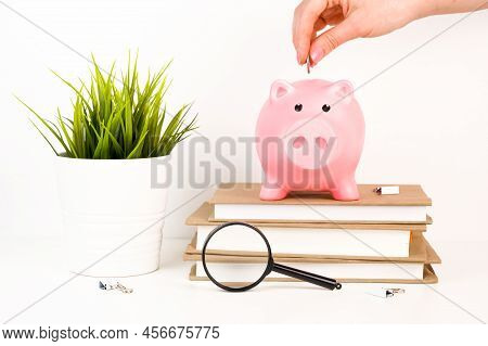Hand Putting Money Into Piggy Bank On Top Of Books. Caot Or Savings For Education