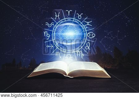 Old Book On Black Surface And Illustration Of Zodiac Wheel With Astrological Signs Under Starry Sky 