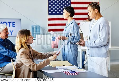 Side View Portrait Of Young Black Woman Taking Voting Ballot On Election Day With American Flag In B