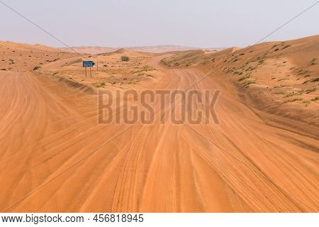 Wahiba Sands, Oman - 04.03.2018: Fork In The Dirt Road In The Desert With Blue Road Sign Pointing To
