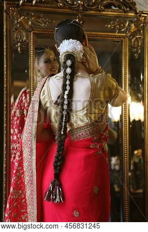 Female Model Indian Bride In Saree, Wearing Gold And Jasmine Flower Garlands In The Hair Near Mirror