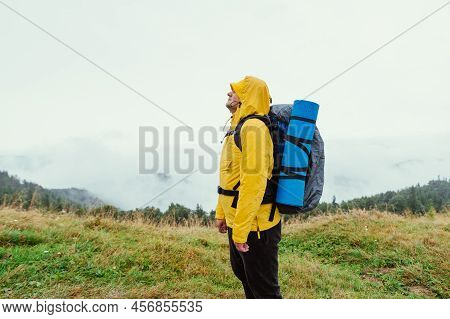 Man In A Yellow Raincoat In A Mountain Hike In Rainy Weather On A Background Of Landscapes With Clou