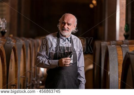 Caucasian Senior Graybeard Winemaker Tasting Red Wine To Ascertain Their Quality And Flavor, Standin