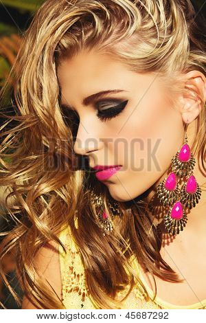 primo piano di donna bionda con i capelli ricci lunghi bagnato indossa rossetto rosa e orecchini d'oro e Rosa neon