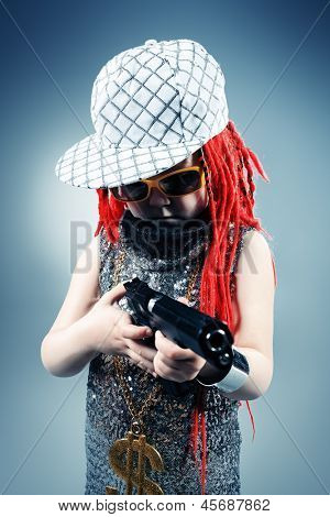Porträtt av en trendig liten tjej bär röda flätor och moderna kläder och hålla en pistol.