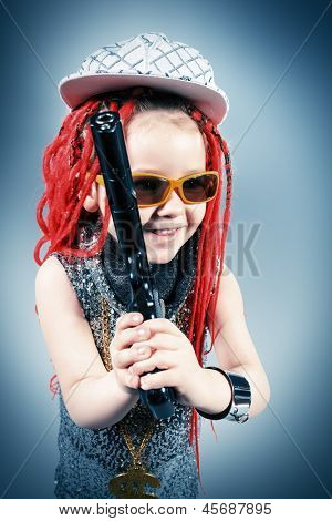 Porträtt av en trendig liten tjej bär röda flätor och moderna kläder och hålla en pistol.