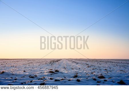 Winter Rural Landscape, A Snowy Agricultural Field Covered With Snow And Ice, At Sunset, In The Bana