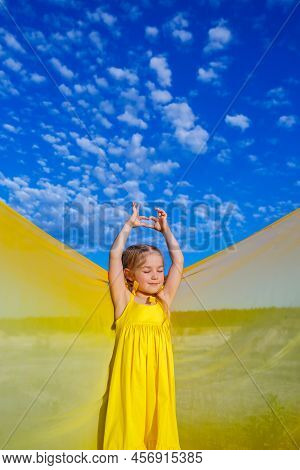 Ukrainian Girl 7 Years Old, She Is A Patriot Of Ukraine, Dressed In A Yellow Dress Against A Blue Sk