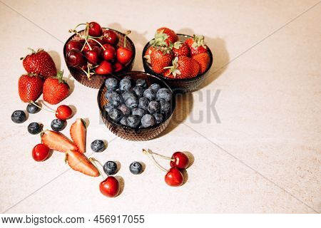 Fruits, Blueberries, Strawberries, Cherries, In Round Glass Plates On A Beige Table. View From Above