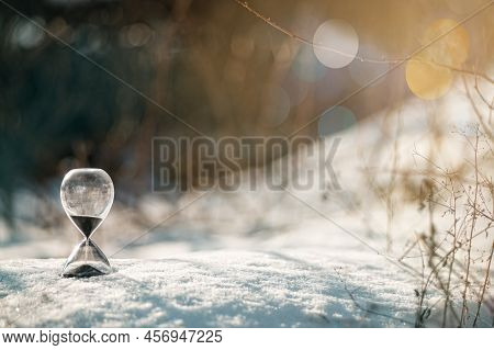 Hourglass As A Symbol Of Changing Of The Seasons. Spring Is Coming. Hourglass In The Grass And Melti