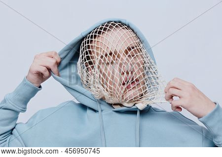 Tortured, Suffering From Problems, A Man With A Mesh On His Face Stands In A Light Blue Hoodie On A 