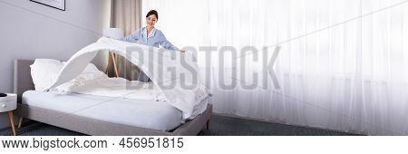 Smiling Young Female Housekeeper Arranging Bedsheet On Bed In Hotel Room