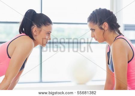 Close-up side view of two angry young women staring at each other at a bright gym