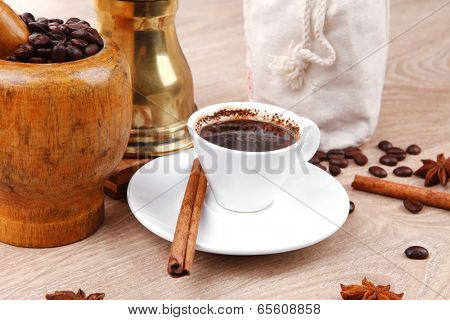 sweet hot drink : black turkish coffee in small white mug with mortar and pestle , coffee beans in white bag , copper old style cezve full hot coffee, decorated with cinnamon sticks and anise stars