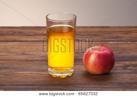 Glass of apple juice and red apple on wooden background