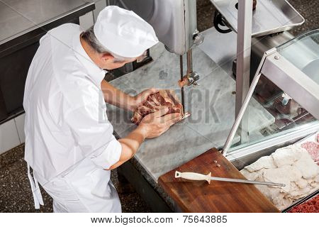 High angle view of butcher cutting meat with bandsaw in butchery