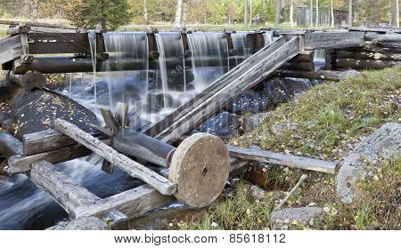 A grindstone connected to water power in an old wooden construction.