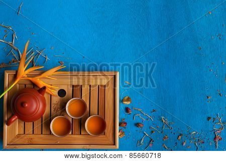 Clay Teapot, Three Teacups And Yellow Flower With Shuck On Blue Wooden Background.