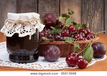 The Jar Of Homemade Fruits Jam With Plums And Cherries In Basket On Rustic Wooden Background