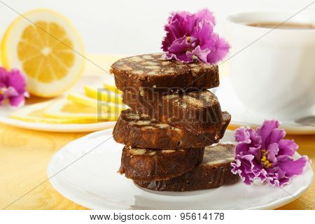 Pile Of Delicious Chocolate Cake Slices With The Cookies Filling, Decorated Violet Flowers On A Whit