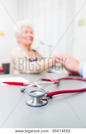 Doctor sitting with pensioner in surgery consultation hour at desk