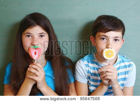 two marshmellow candy on stick designed as fruit orange and strawberry with smiling happy kids girl and boy on the background