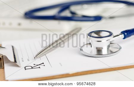 Prescription Form Clipped To Pad Lying On Table With Stethoscope And Silver Pen